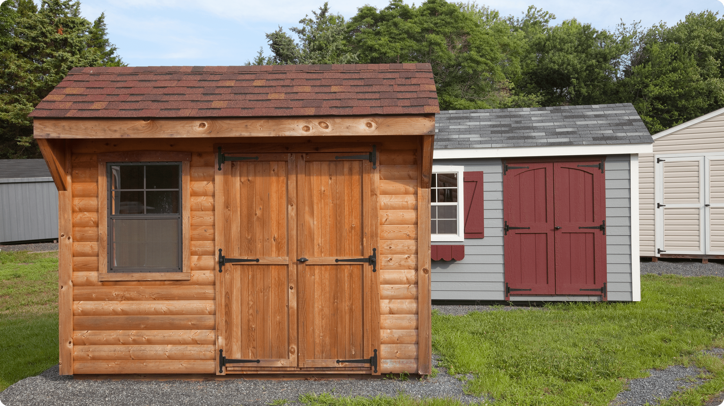 Wooden sheds on grass with trees behind.
